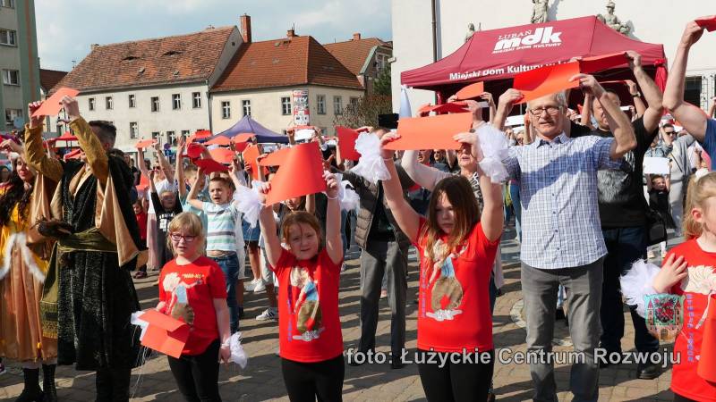 uczestnicy pikniku śpiewający hymn Polski i trzymający kartki w kolorze białym i czerwonym w celu utworzenia flagi